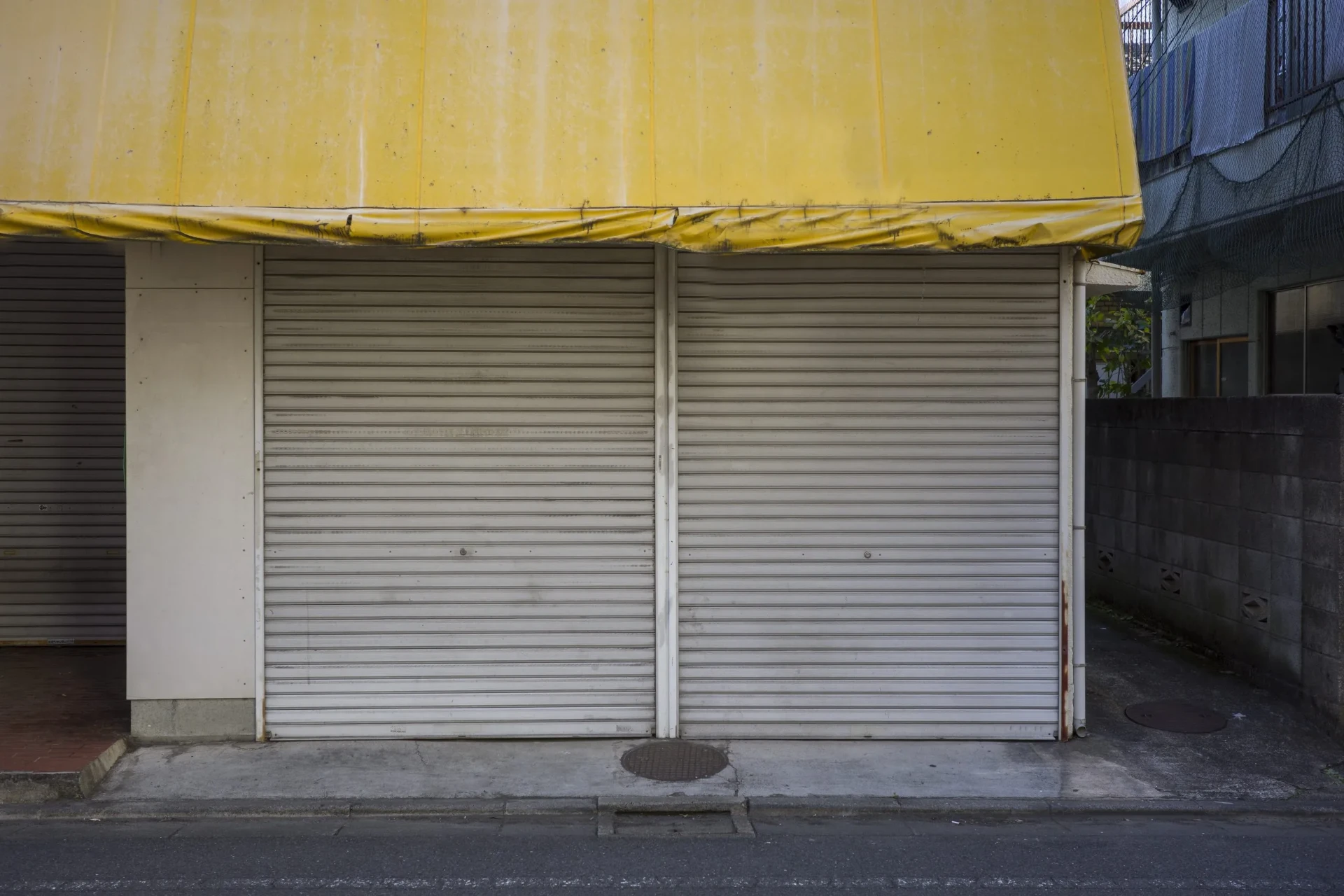 Shuttered shop with a faded yellow awning.